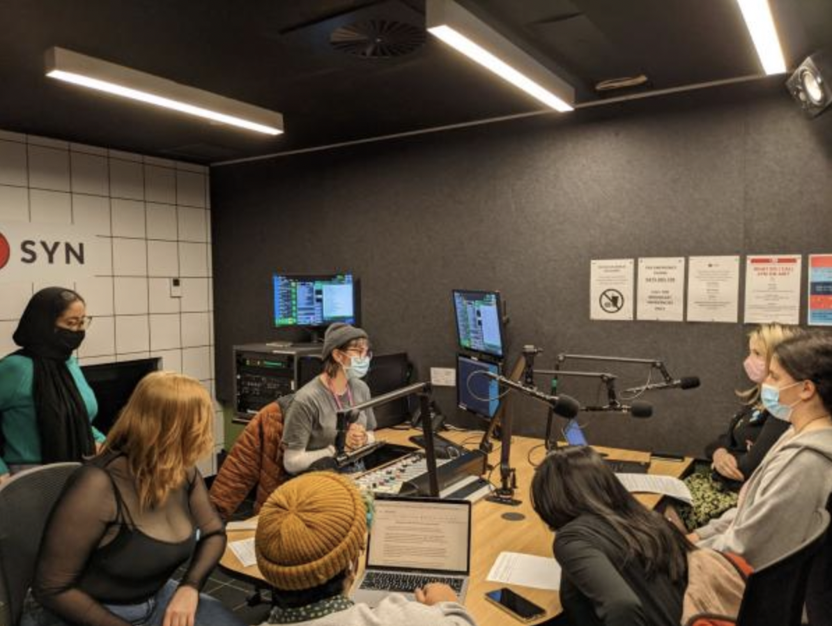 Photo of a group of young people sitting at a radio table with microphones and screens 
